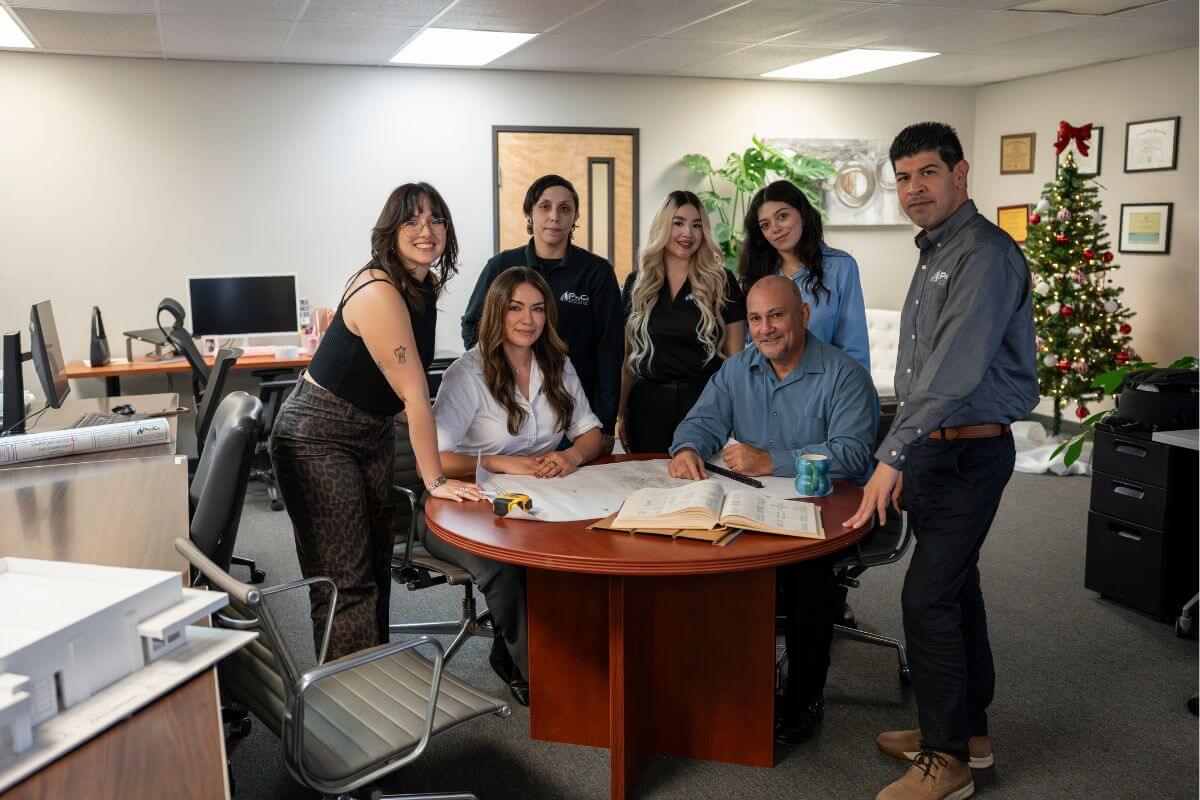 Team gathered around a circular table discussing blueprints and project documents in the office.