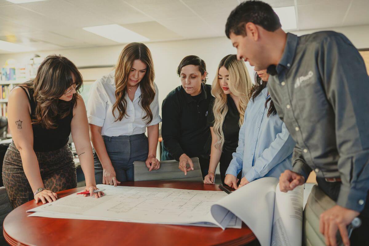 Team members collaborating around a table while reviewing architectural plans in the office.